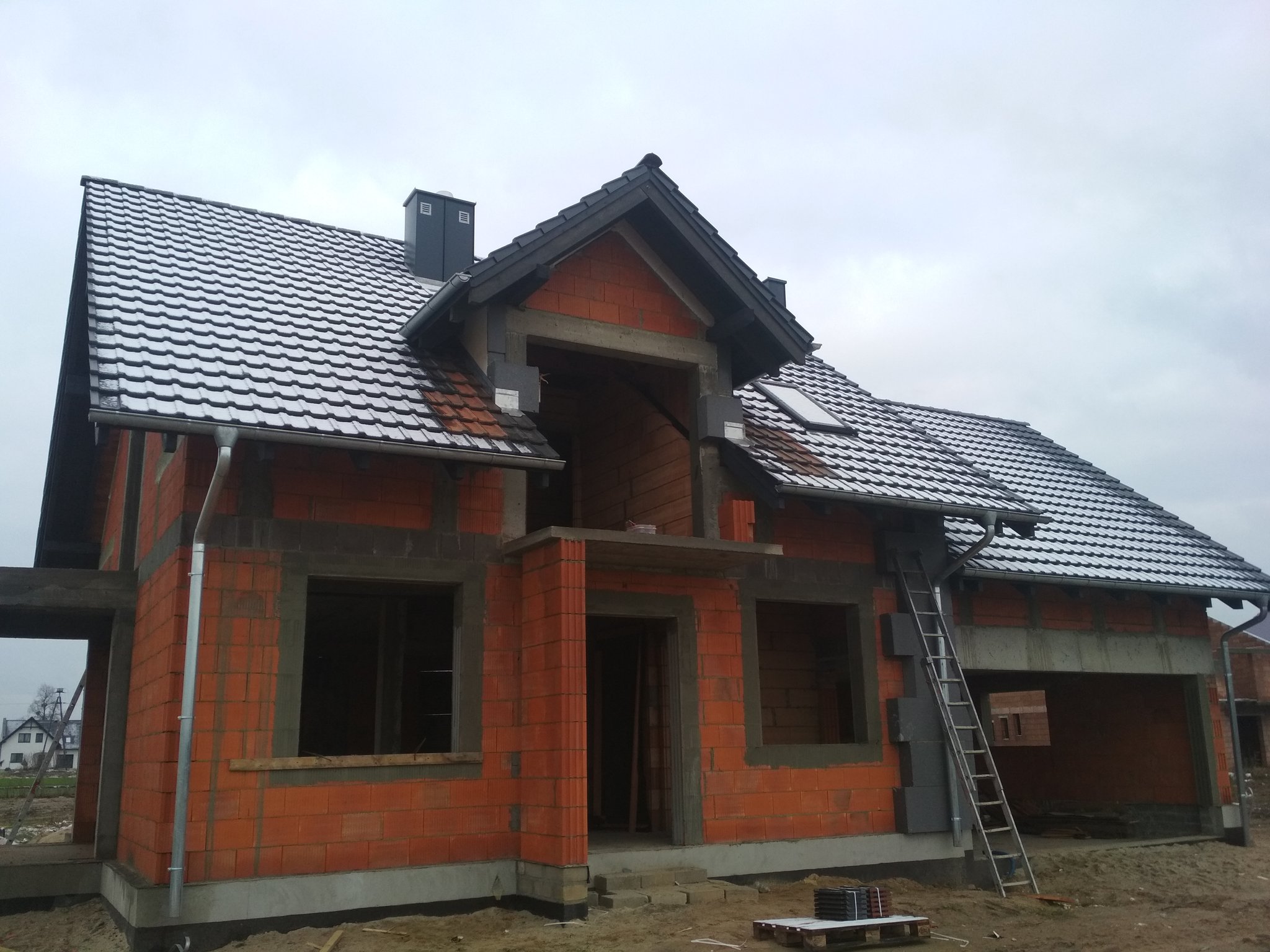 Dom z ukończonym ciemnym pokryciem dachu i lukarną