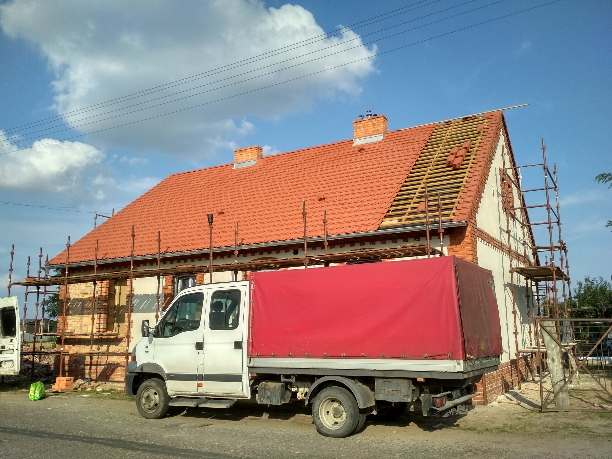 Dach w trakcie krycia — nowa dachówka i rusztowanie przy szczycie