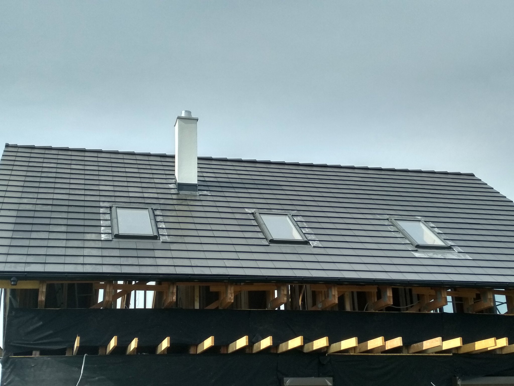 Gotowy dach z kominem i trzema oknami dachowymi przy pochmurnym niebie