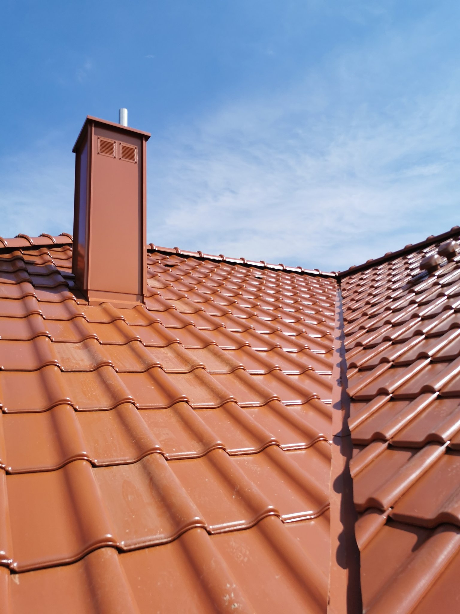 Zbliżenie czerwonej dachówki i obudowanego komina