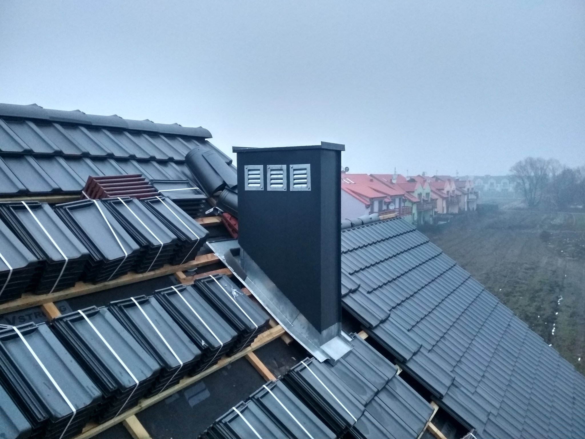 Ciemna dachówka przy obudowanym kominie w trakcie krycia