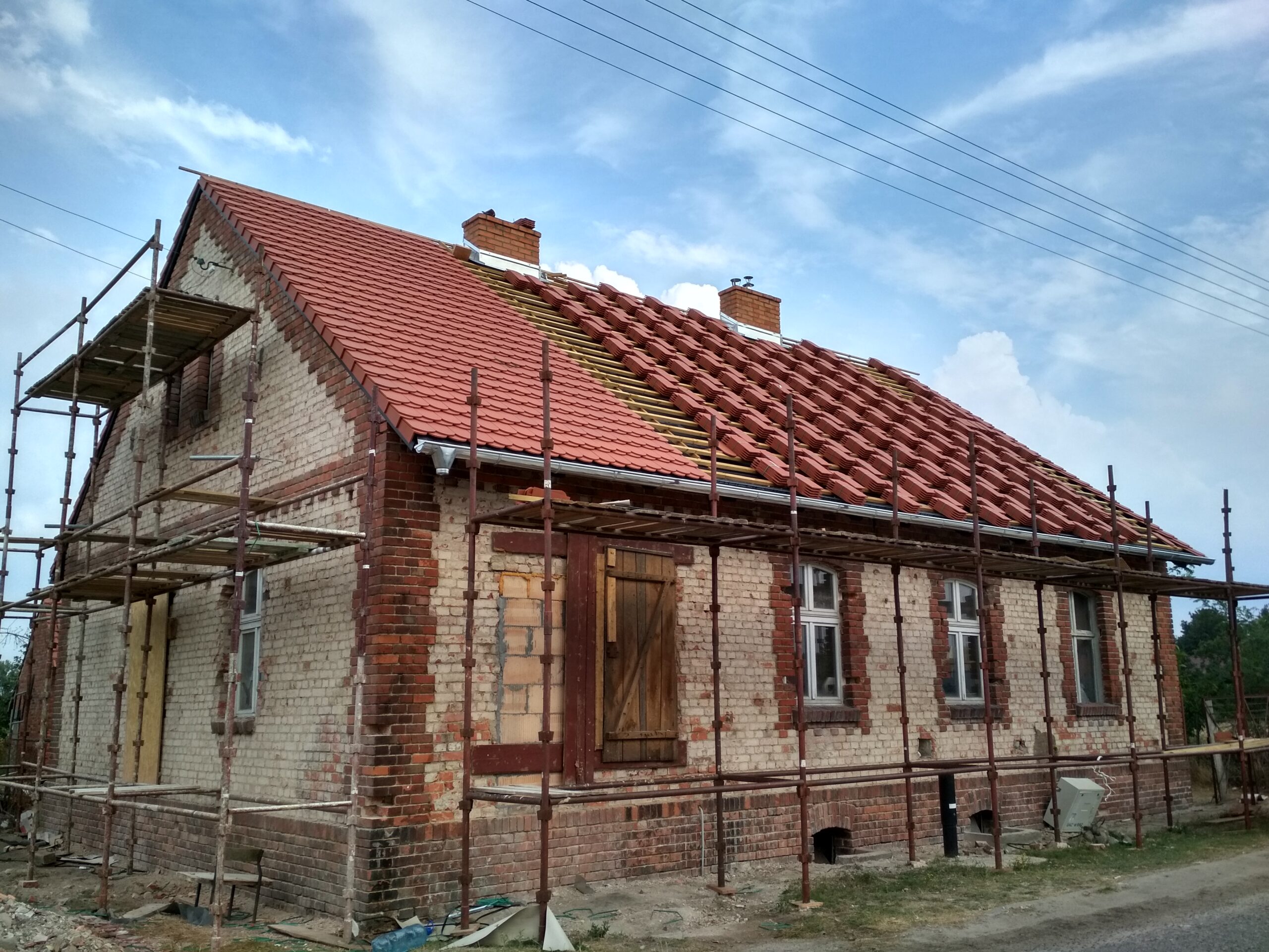 Układanie nowej czerwonej dachówki na połaci
